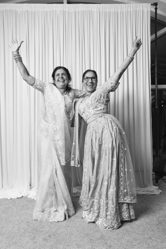 Two women in saris throw their arms up in celebration